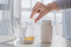 healthy-lifestyle-medicine-nutritional-supplements-and-people-concept-close-up-of-male-hands-holding-pills-with-cod-liver-oil-capsules-and-water-glass